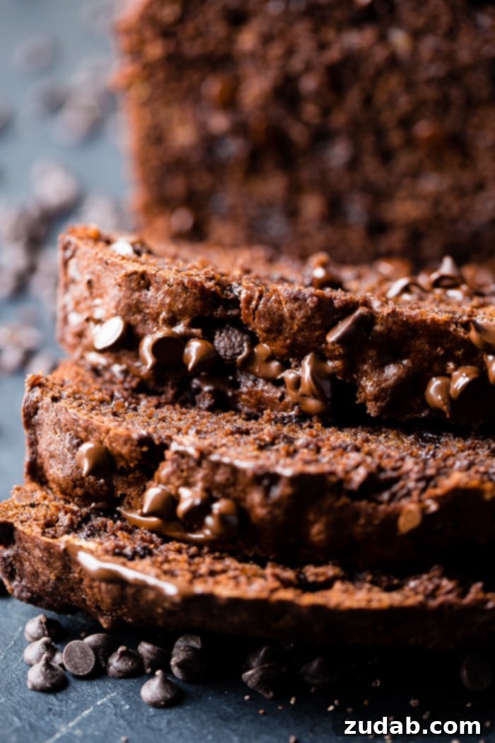 Ultimate Double Chocolate Banana Bread 5 Several slices of double chocolate banana bread arranged on a dark board, surrounded by melted chocolate and mini chocolate chips, highlighting the bread's rich color and gooey chocolate content.
