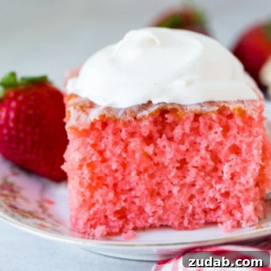 Wobbly Strawberry Dream Cake 3 A floral china plate with a slice of pink strawberries and cream jello cake with a dollop of whipped cream on top, a strawberry behind the cake and a red checkered napkin beside it.