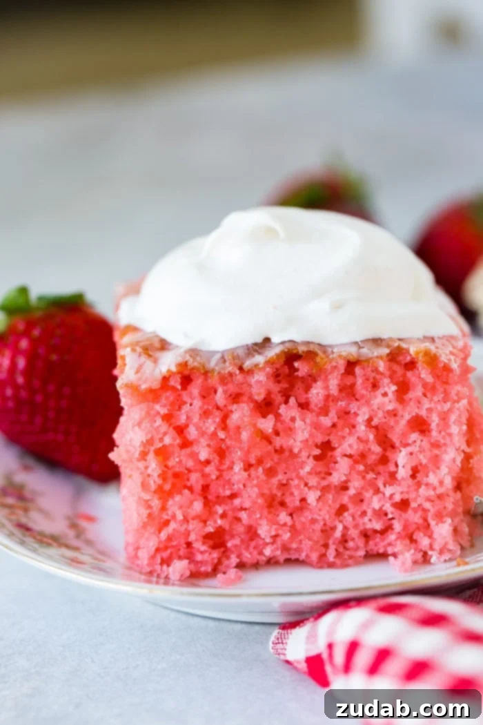 Wobbly Strawberry Dream Cake 5 A floral china plate with a slice of pink strawberries and cream jello cake with a little cool whip on top and strawberries behind it.