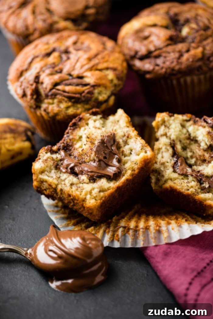 Nutella-Marbled Banana Muffins 5 Nutella swirled banana muffins surrounding a cut-open muffin revealing the gooey Nutella center, with a spoonful of Nutella in the foreground, enticing and delicious.