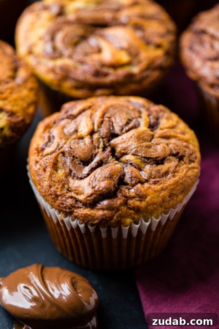 Nutella-Marbled Banana Muffins 6 A Nutella swirled banana muffin surrounded by more delicious muffins, highlighting the irresistible texture and enticing swirl.