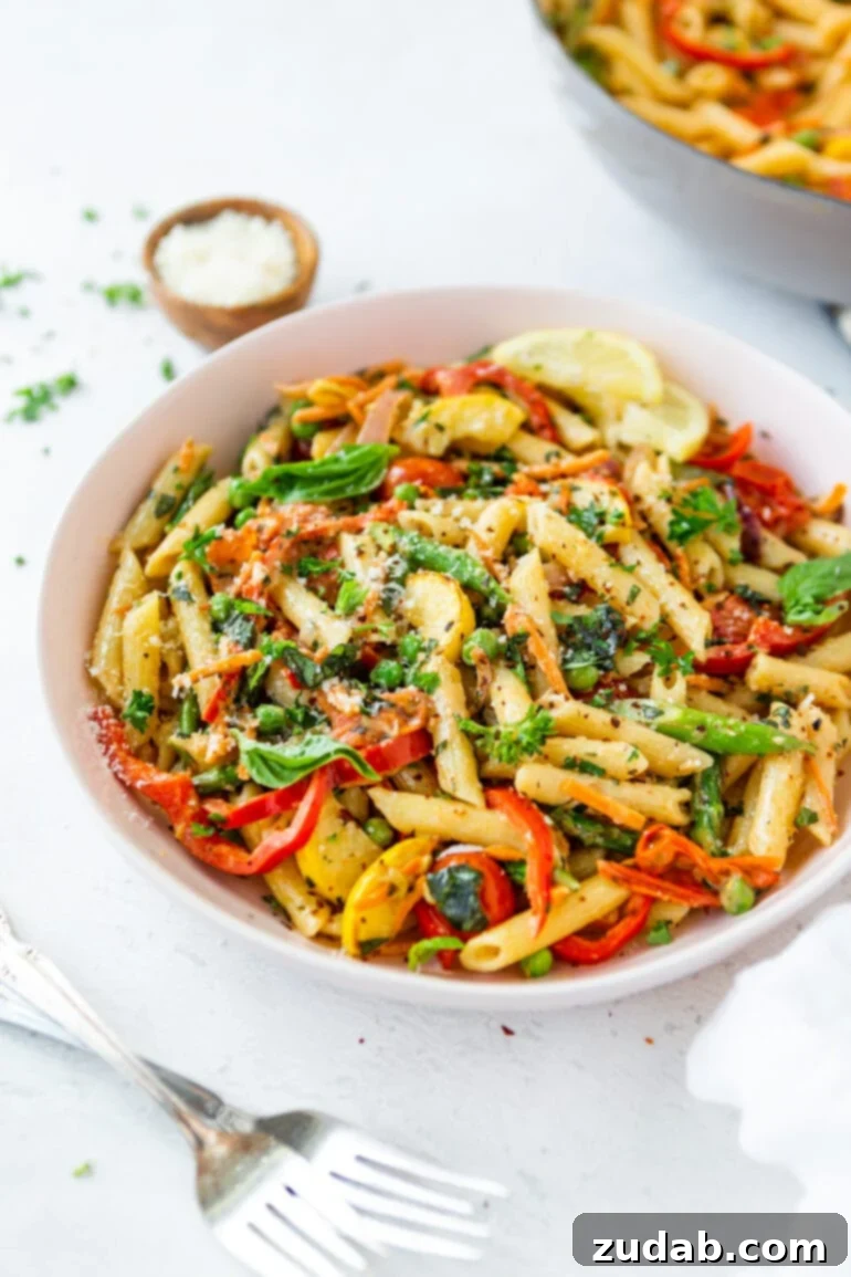 A large white serving bowl overflowing with al dente penne pasta, generously mixed with colorful fresh vegetables and garnished with grated Parmesan cheese.