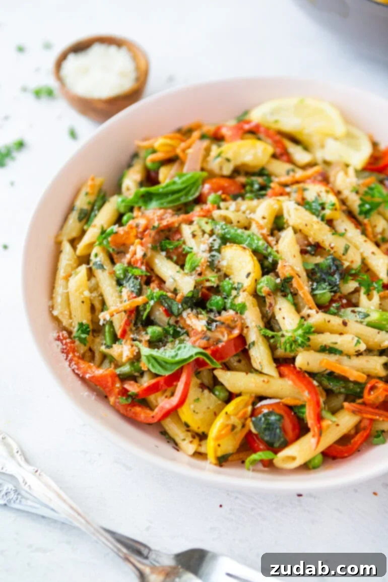A close-up of a bowl of Pasta Primavera, featuring perfectly cooked penne pasta, vibrant red bell peppers, sliced yellow squash, red onions, and fresh herbs, highlighting the rich textures and colors.