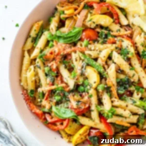 A photo of a large bowl full of penne pasta tossed with vegetables and a creamy sauce