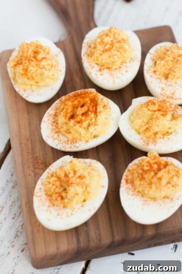 The Best Deviled Eggs Recipe you'll ever make has a few secret ingredients like, vinegar, and paprika! These are the ONLY deviled eggs we make now! Seven of the best Deviled Eggs on a wooden platter on top of a white wooden table.