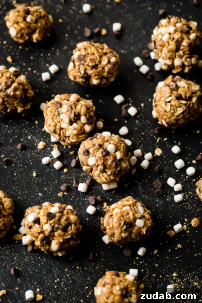 No Bake Smores Protein Power Bites 7 Overhead view of Protein No Bake S'mores Energy Bites scattered on a dark surface, artfully interspersed with mini marshmallows, chocolate chips, and graham cracker crumbs, highlighting the key ingredients.