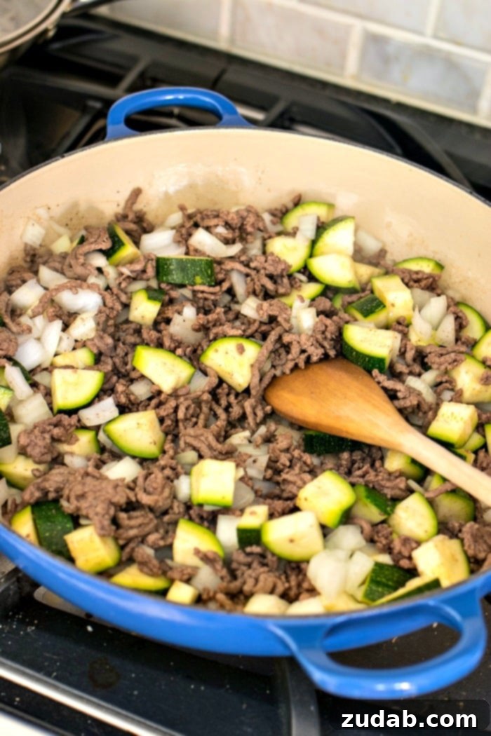 Simple & Satisfying Beef Ragu Pasta 6 Ingredients for easy beef ragu and pasta displayed on a cutting board, including zucchini, diced tomatoes, ground beef, and onions.