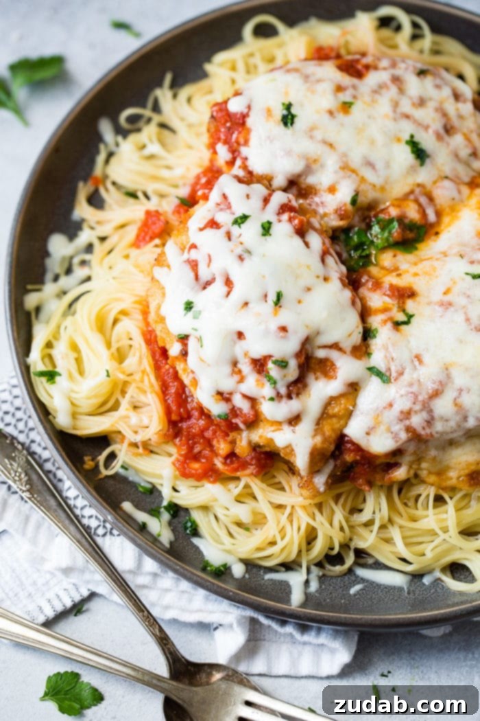 Speedy Weeknight Chicken Parmesan 5 A dark grey platter generously filled with tender angel hair pasta, a vibrant marinara tomato sauce, golden-brown breaded chicken cutlets topped with more marinara and melted, gooey mozzarella cheese, finished with a sprinkle of fresh chopped Italian flat-leaf parsley. This quick and easy shortcut chicken parmesan is ideal for busy weeknights.