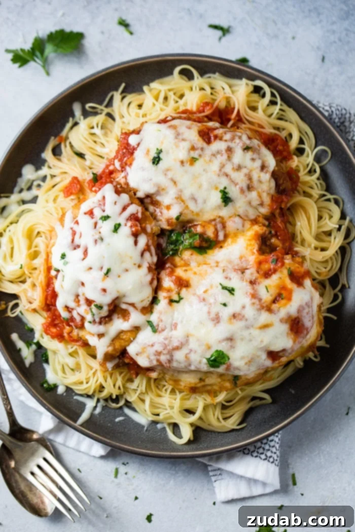 Speedy Weeknight Chicken Parmesan 6 A dark grey platter generously filled with tender angel hair pasta, a vibrant marinara tomato sauce, golden-brown breaded chicken cutlets topped with more marinara and melted, gooey mozzarella cheese, finished with a sprinkle of fresh chopped Italian flat-leaf parsley. This quick and easy shortcut chicken parmesan offers ultimate weeknight satisfaction.