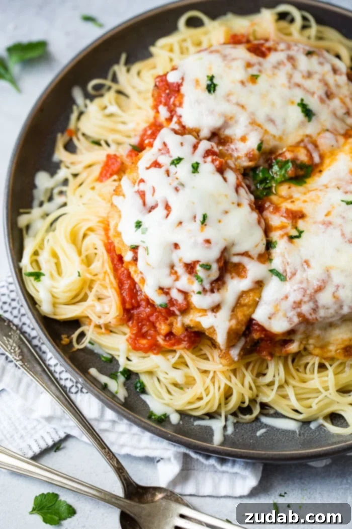 Speedy Weeknight Chicken Parmesan 7 A dark grey platter generously filled with tender angel hair pasta, a vibrant marinara tomato sauce, golden-brown breaded chicken cutlets topped with more marinara and melted, gooey mozzarella cheese, finished with a sprinkle of fresh chopped Italian flat-leaf parsley. This quick and easy shortcut chicken parmesan is perfect for a delicious weeknight meal.