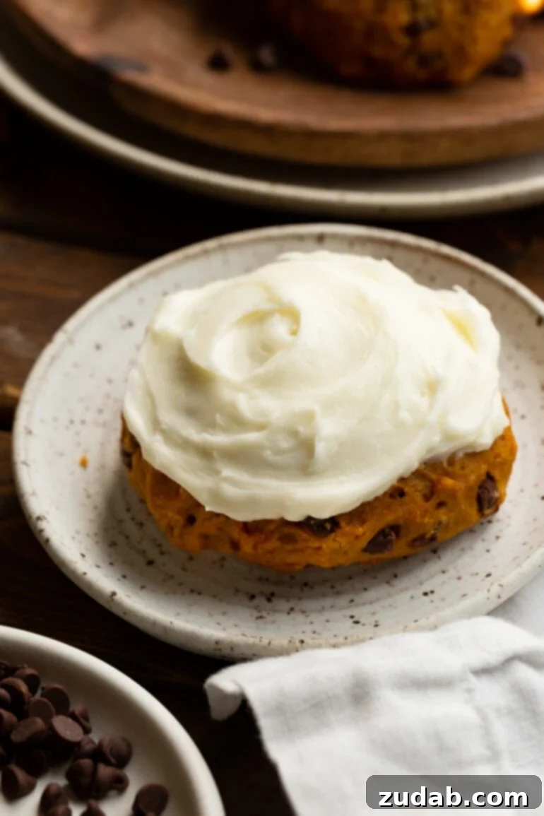 Cozy Pumpkin Chocolate Chip Cookies with Cream Cheese Frosting 3 a photo of a thick pumpkin chocolate chip cookie topped with cream cheese frosting sitting on a small dessert plate