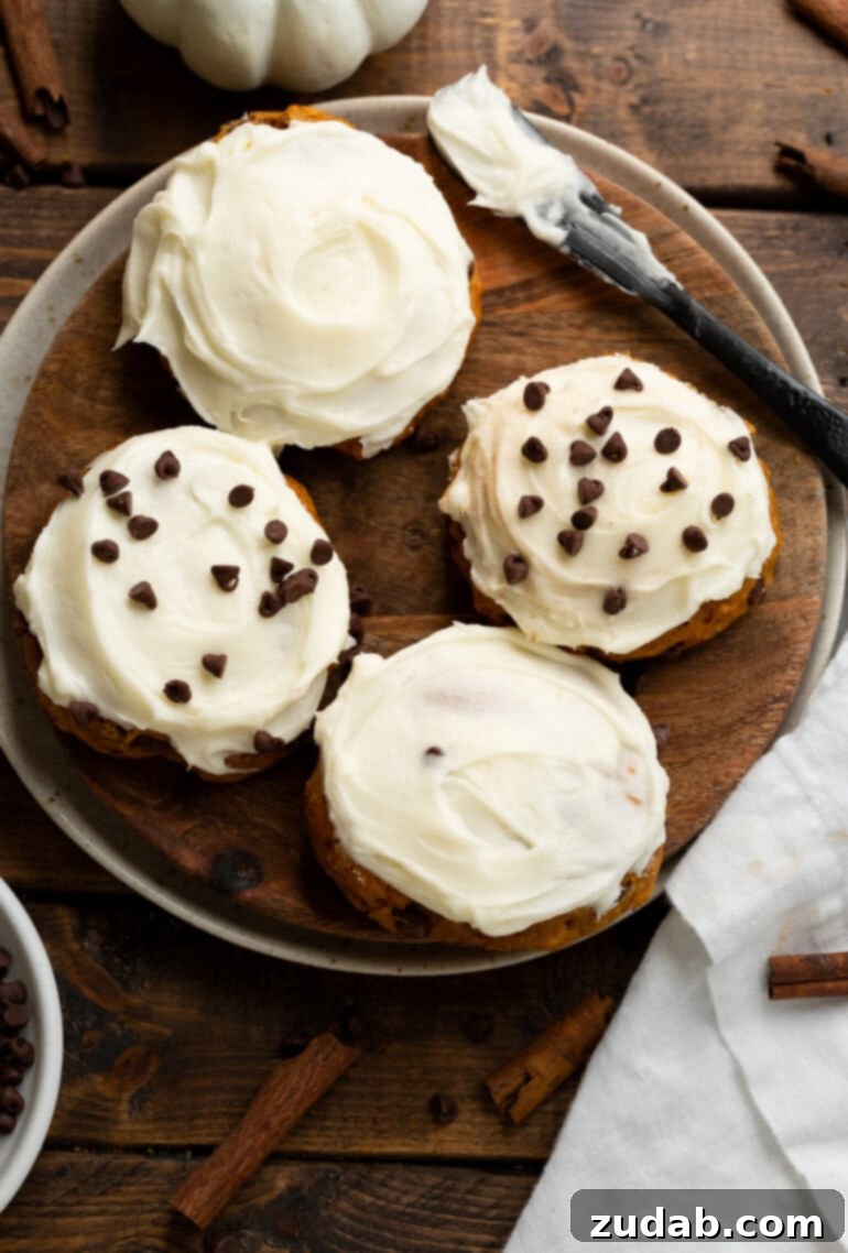 Cozy Pumpkin Chocolate Chip Cookies with Cream Cheese Frosting 4 a photo of a wooden serving tray with four cookies on it frosted with cream sheet frosting and two of the cookies topped with mini chocolate chips