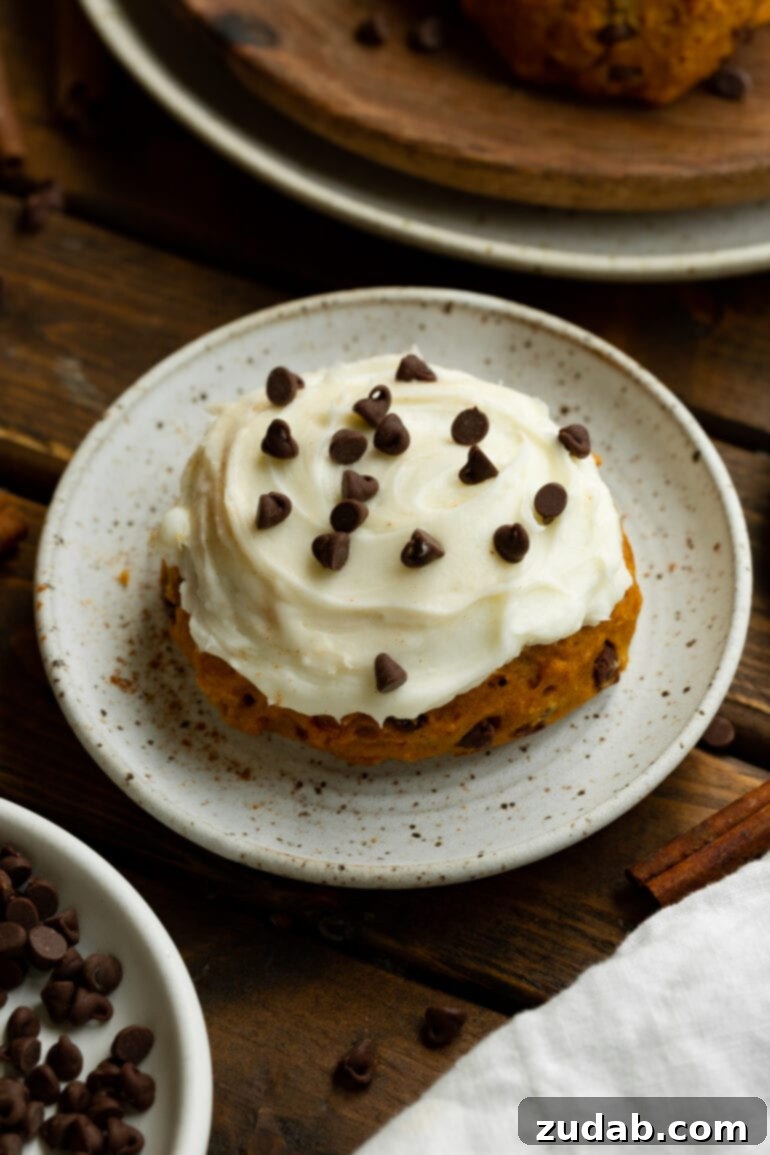 Cozy Pumpkin Chocolate Chip Cookies with Cream Cheese Frosting 7 a photo of a single thick pumpkin chocolate chip cookie frosted with cream cheese frosting and sprinkled with mini chocolate chips