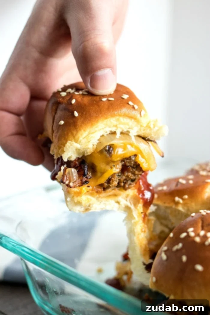 Effortless Smoky BBQ Meatball Sliders 2 A hand pulling a delicious BBQ meatball slider from a baking tray, showcasing its layers of cheese, bacon, and onion between sweet Hawaiian rolls.