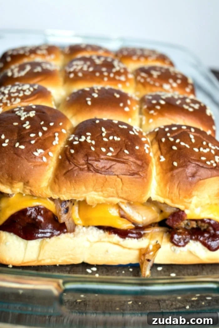 Effortless Smoky BBQ Meatball Sliders 3 Close-up of a baking dish filled with assembled BBQ meatball sliders, showing the tops of the rolls brushed with butter and sprinkled with sesame seeds.