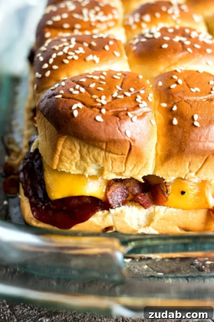 Effortless Smoky BBQ Meatball Sliders 4 A close-up of BBQ meatball sliders being assembled in a clear Pyrex baking dish, featuring layers of Hawaiian rolls, sauced meatballs, and cheddar cheese slices.