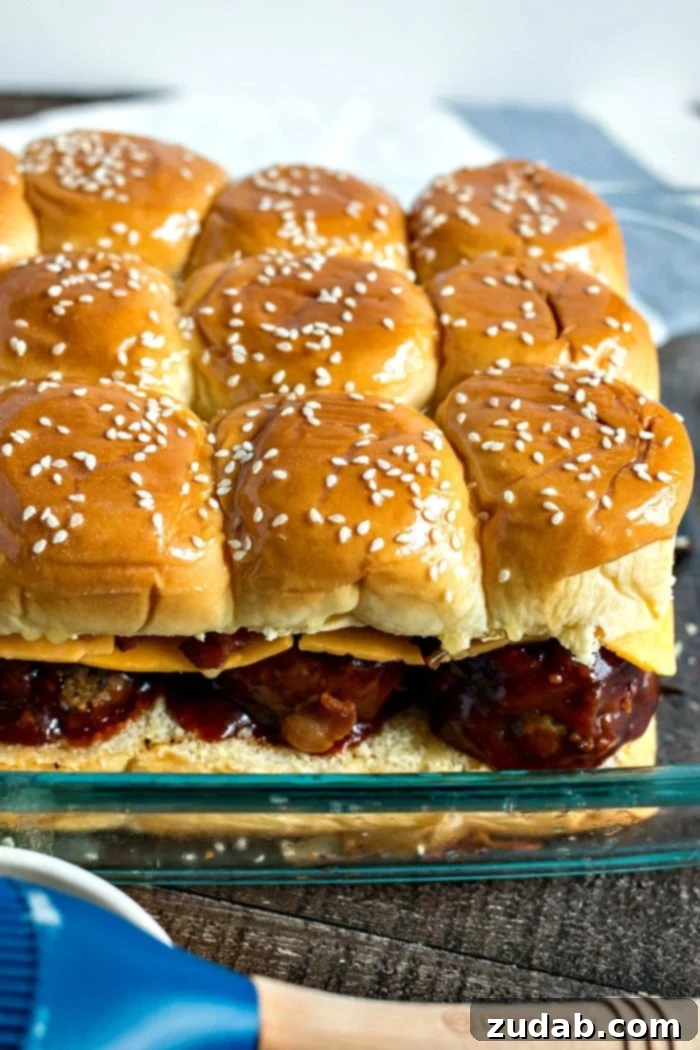 Effortless Smoky BBQ Meatball Sliders 9 Unbaked BBQ meatball sliders arranged neatly in a Pyrex baking dish, topped with butter and sesame seeds, ready to go into the oven.