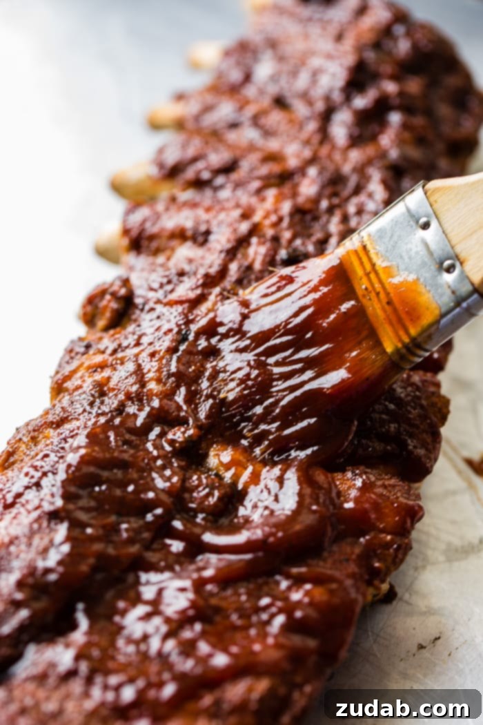 Fall-Off-The-Bone Instant Pot BBQ Ribs 2 A baking sheet with a succulent rack of Smoky BBQ Instant Pot Ribs being generously basted with a rich barbecue sauce, highlighting their irresistible glaze and tenderness.
