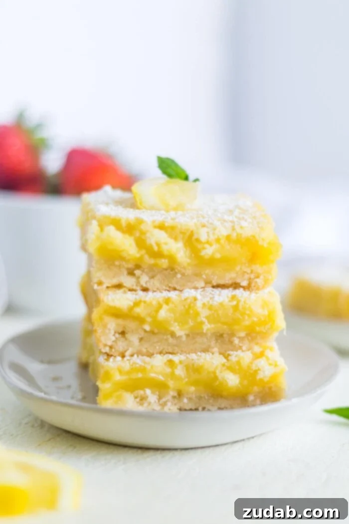 lemon bars a photo of three lemon bars stacked on each other with a thick butter crust and creamy lemon filling topped with powdered sugar