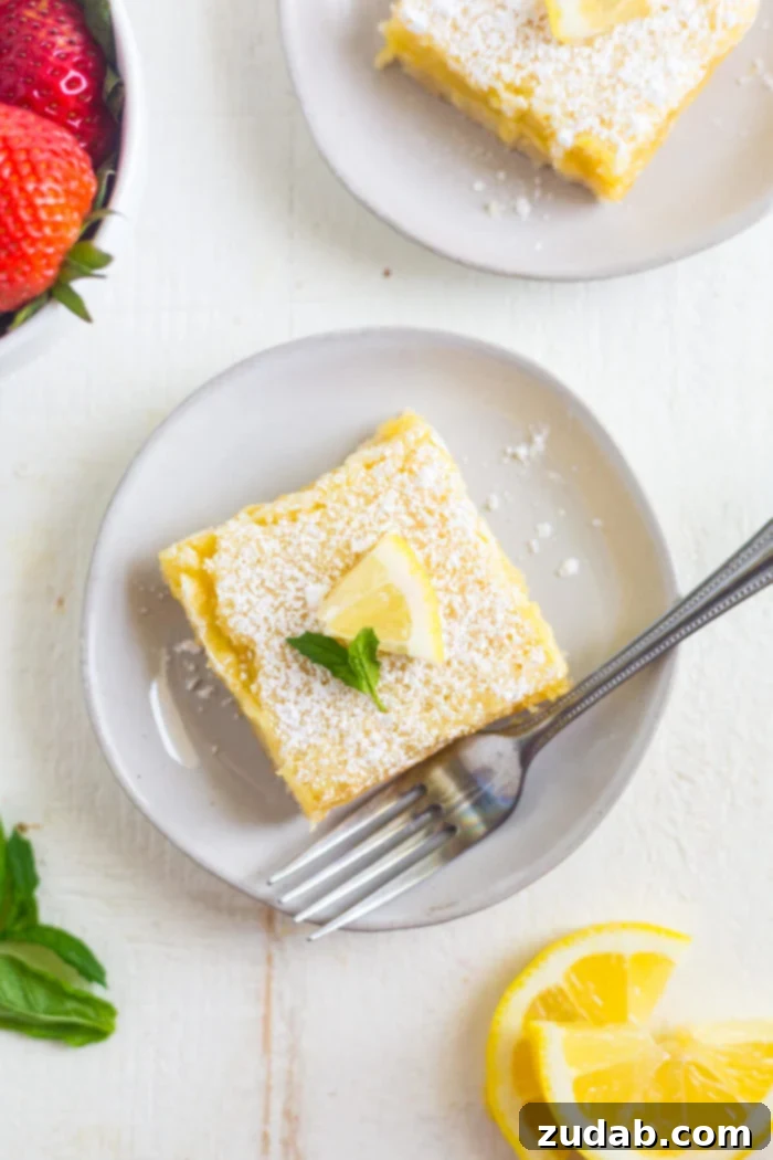 lemon bars recipe a photo taken over the top of a single square lemon bar sitting on a small dessert plate with a silver fork sitting next to it
