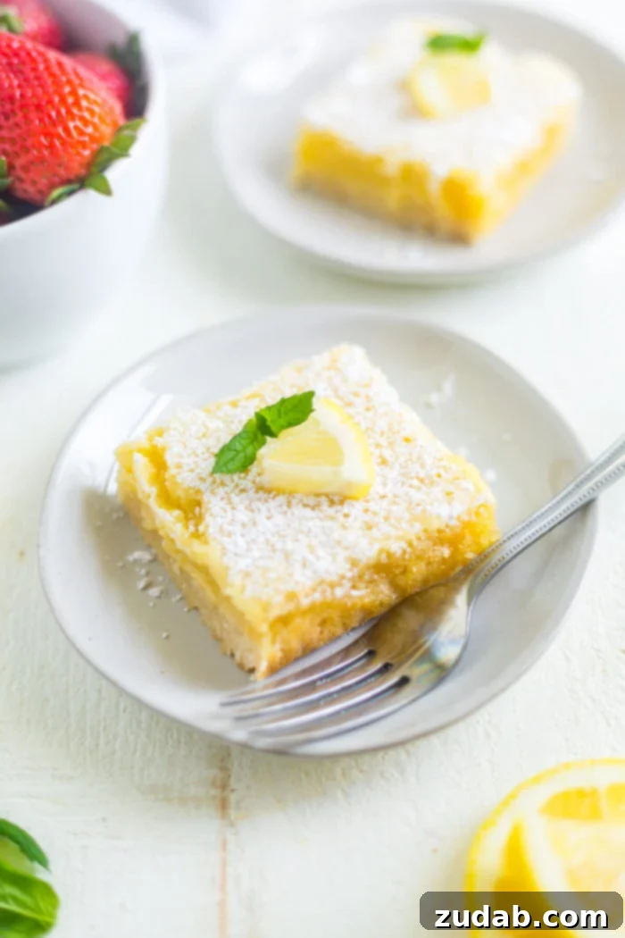 recipe for lemon bars a photo of a single square lemon bar topped with powdered sugar and a wedge of lemon sitting on a small white dessert plate with a fork sitting next to it