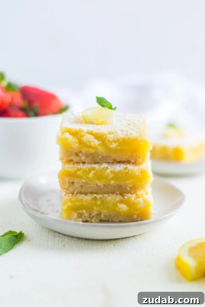lemon bars a photo of three square lemon bars stacked on top of each other sitting on a small white dessert plate