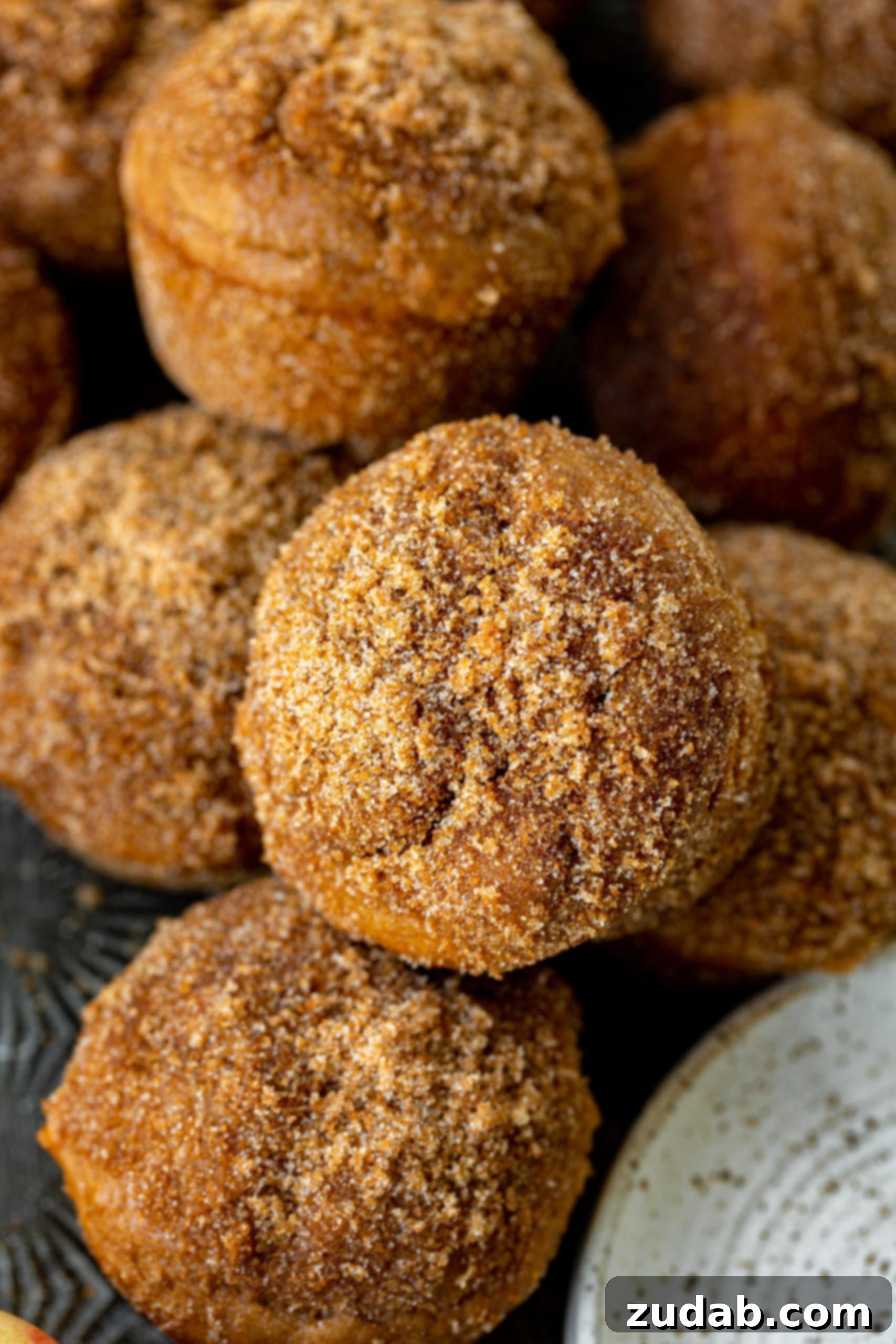 Apple Cider Donut Muffins A photo of several golden, fluffy apple cider donut muffins topped with a glistening cinnamon brown sugar coating, ready to be enjoyed.
