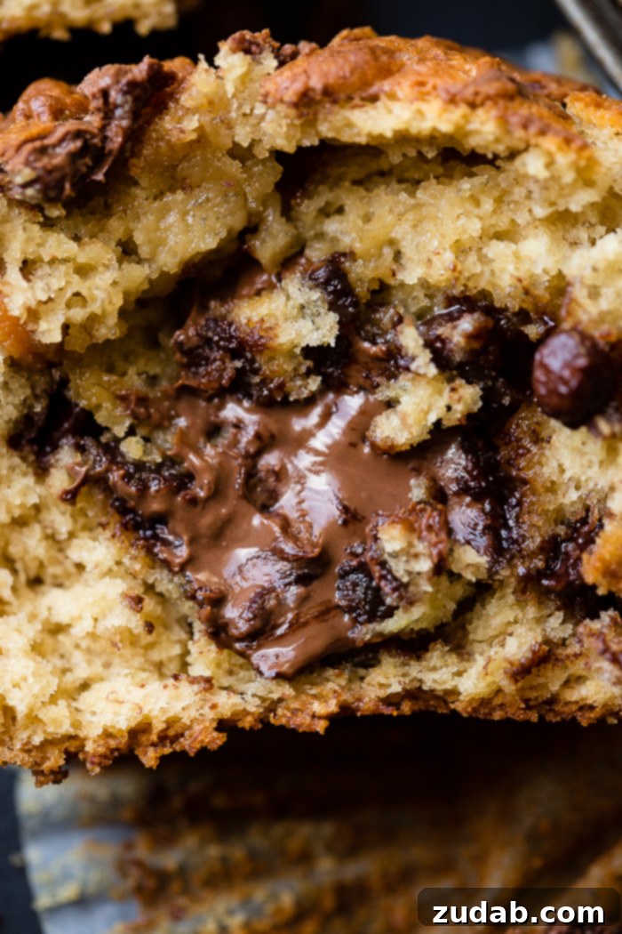 Peanut Butter Banana Muffins with a Gooey Nutella Center 8 A perfectly halved Nutella-stuffed peanut butter banana muffin, showcasing its gooey, chocolate-hazelnut core, resting invitingly on an open muffin liner.