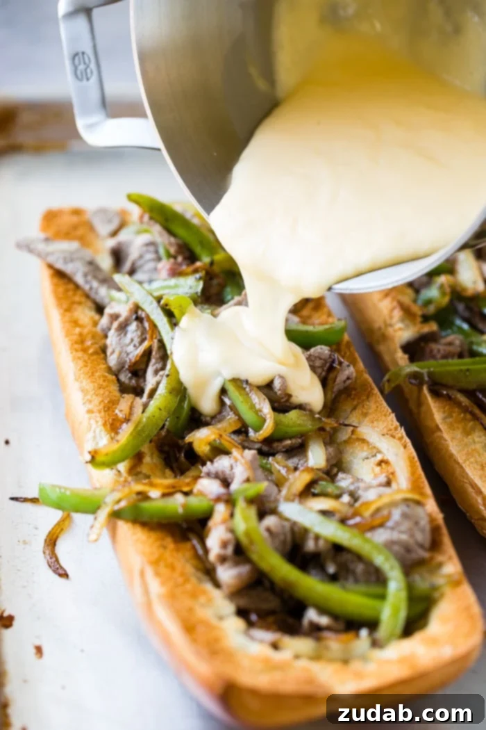 Philly Cheesesteak Pull Apart Bread 2 A golden-crusted French bread loaf, sliced open and generously filled with tender sautéed ribeye steak, vibrant green bell peppers, and caramelized onions, all smothered in a rich, creamy cheese sauce, promising an easy and satisfying Philly cheesesteak experience.