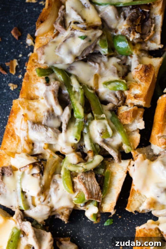 Philly Cheesesteak Pull Apart Bread 3 A close-up shot of an easy Philly Cheesesteak Bread, showcasing the golden-brown French bread crust overflowing with a savory filling of thinly sliced steak, softened green bell peppers, and sweet caramelized onions, generously coated in a luscious cheese sauce, ready to be enjoyed.