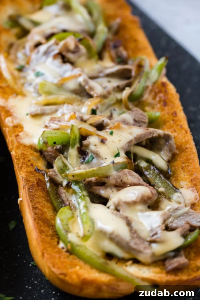 Philly Cheesesteak Pull Apart Bread 4 An open French bread loaf filled with thinly sliced and cooked ribeye steak, green bell peppers, and onions, all generously covered in a creamy, golden cheese sauce, resting on a wooden cutting board, ready to be sliced and served as an easy Philly Cheesesteak Bread.