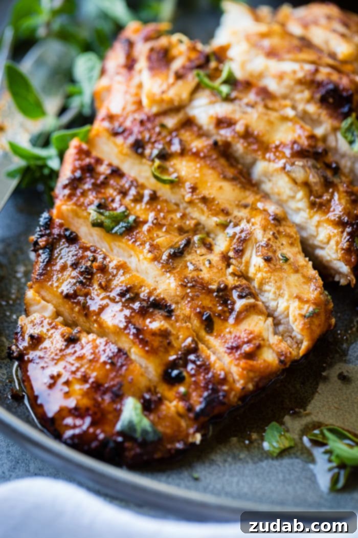 Effortless Oregano Grilled Chicken 2 A grey plate with sliced quick grilled chicken with oregano, fresh oregano sprigs, and grilled lemon halves behind it.