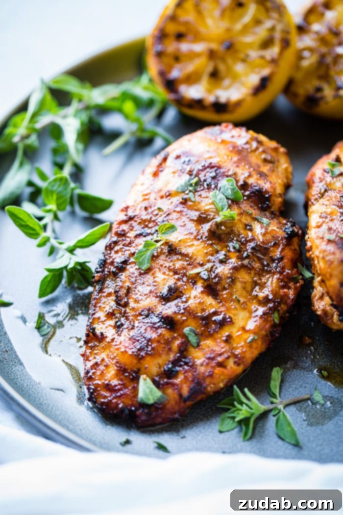 Effortless Oregano Grilled Chicken 5 A grey plate with sliced quick grilled chicken with oregano, fresh oregano sprigs, and grilled lemon halves behind it, resting on a white napkin.