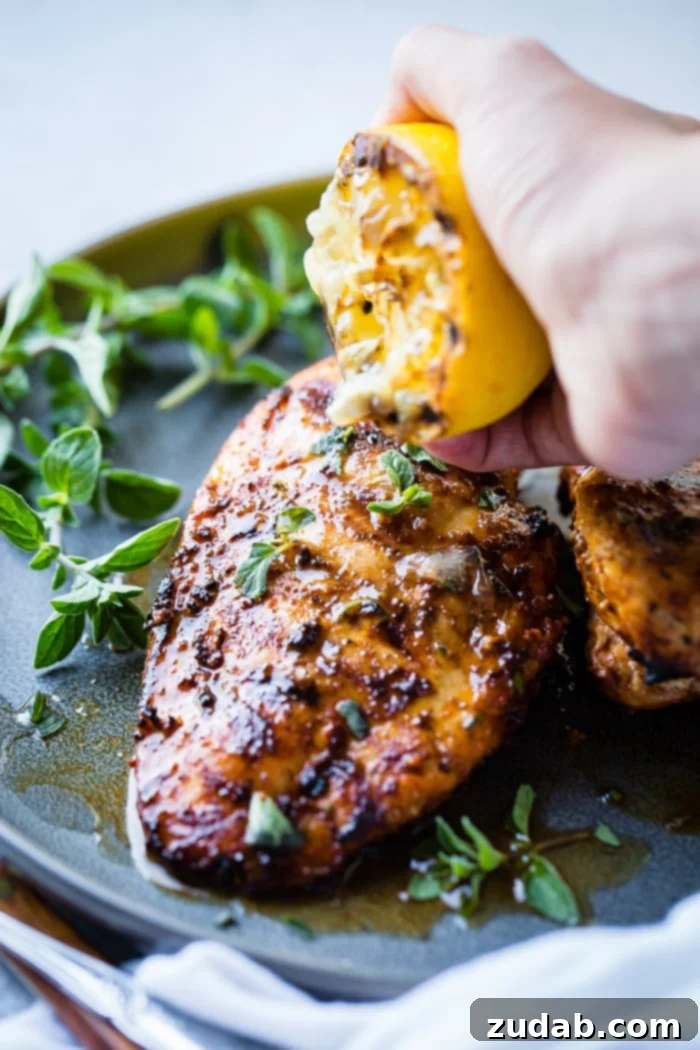 Effortless Oregano Grilled Chicken 6 A grey plate with a sliced quick grilled chicken with oregano, with fresh oregano and a grilled lemon being squeezed over the meat for extra flavor.