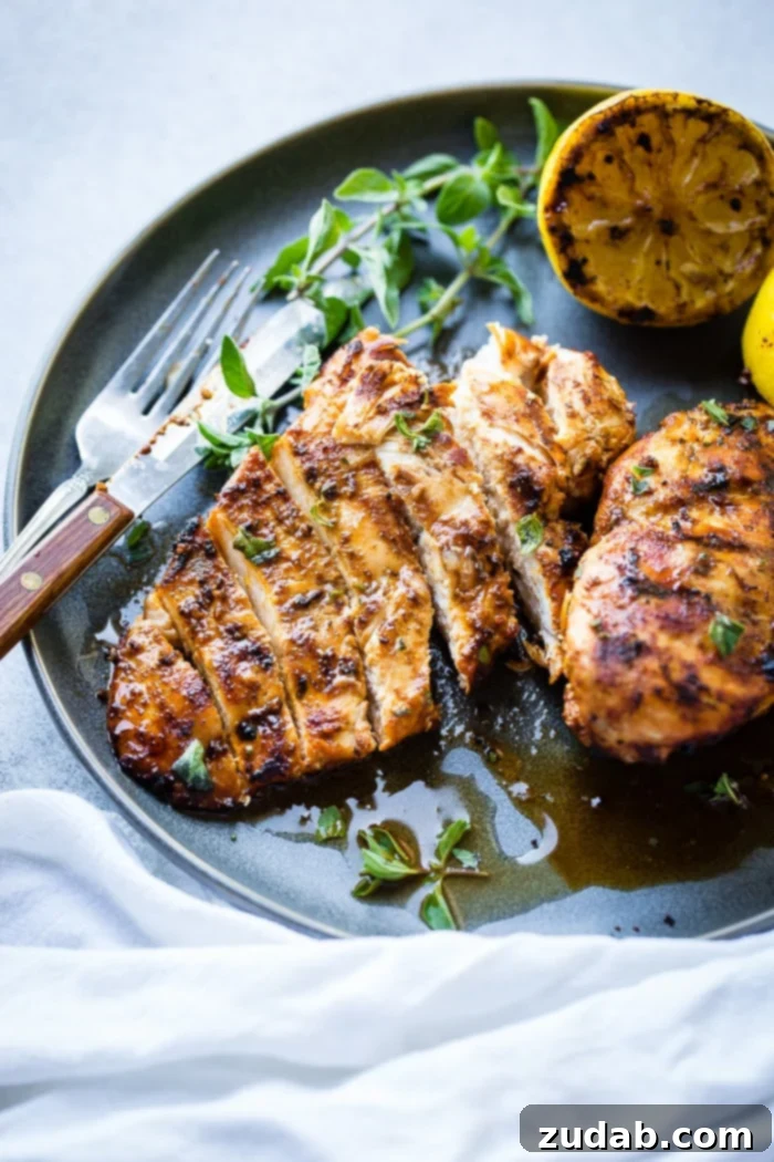 Effortless Oregano Grilled Chicken 7 A grey plate with sliced quick grilled chicken with oregano, fresh oregano sprigs, and grilled lemon halves behind it, resting on a white napkin.