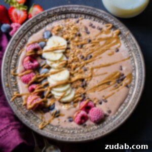 A beautifully presented chocolate banana smoothie bowl, garnished with a medley of fresh berries, banana slices, and a rich peanut butter drizzle.
