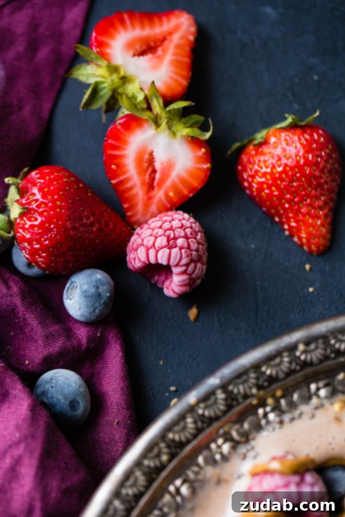 Chocolate Banana Smoothie Bowl Kids Love 6 A visually appealing arrangement of fresh and frozen berries, including blueberries, raspberries, and strawberries, artfully displayed on a black board with a purple napkin, perfect for smoothie bowl toppings.
