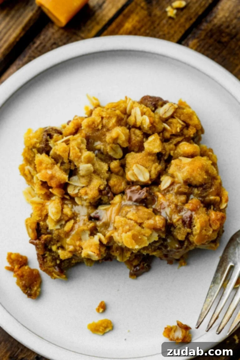 A photo taken above a single Carmelita bar, showcasing its golden crumble topping with visible gooey caramel and silky chocolate beneath, resting on a small white dessert plate.