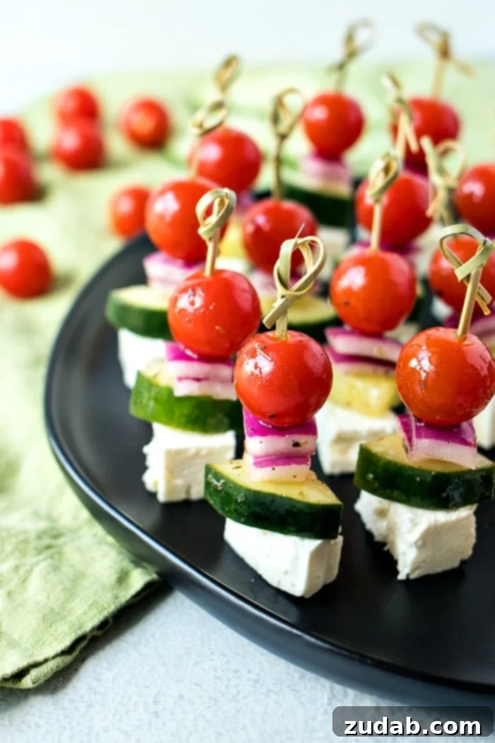Mediterranean Mezze Skewers 2 Bright Greek Salad Skewers with cherry tomatoes, cucumber, red onion, and feta cheese, drizzled with homemade vinaigrette, ready for serving.