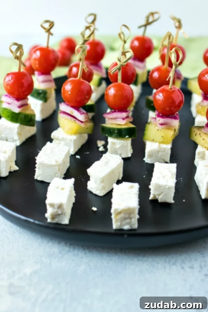 Mediterranean Mezze Skewers 6 Beautifully arranged Greek Salad Skewers, with vibrant colors of tomatoes, cucumber, red onion, and feta, presented on a white serving dish.