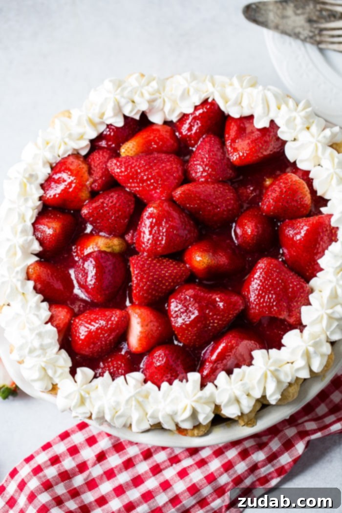 Full Strawberry Pie with Stabilized Whipped Cream a white background with a red and white checkered napkin sitting under a whole fresh strawberry pie with stabilized whipped cream piped around the edges