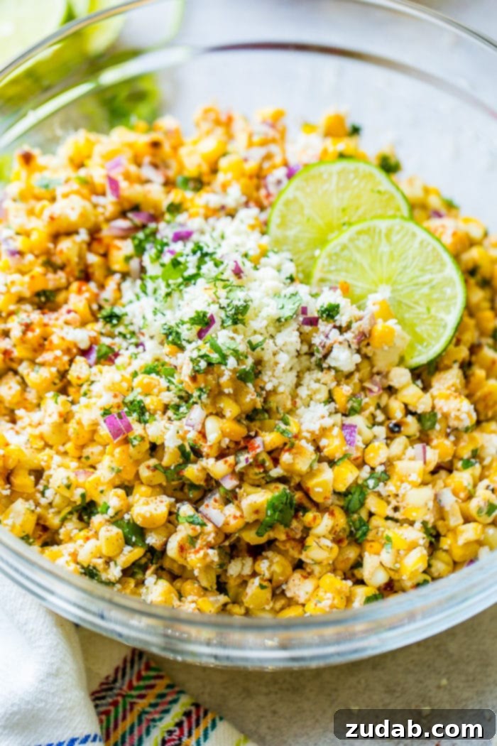 Grilled Elote Corn Salad 4 A generous serving of Grilled Mexican Corn Salad, beautifully arranged in a bowl, showcasing vibrant grilled corn kernels, crisp red onions, fresh cilantro, a creamy coating of crema, crumbled cotija cheese, and a hint of zesty lime juice. This image perfectly captures the rich textures and colors of this popular BBQ side dish.