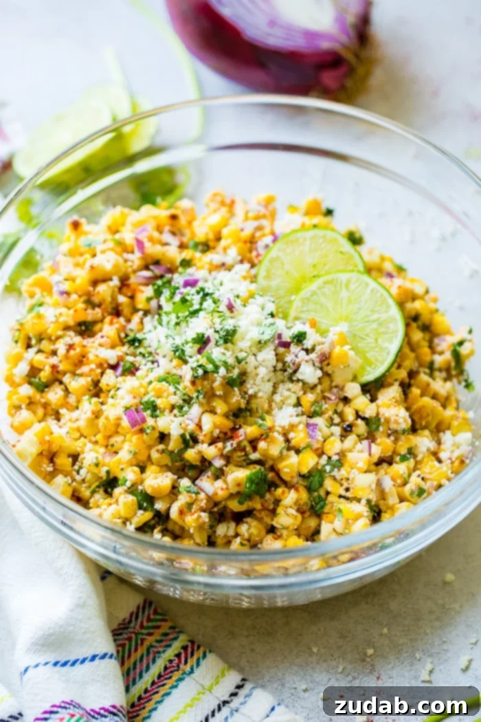 Grilled Elote Corn Salad 5 A close-up shot of a glass bowl brimming with Grilled Mexican Corn Salad, featuring golden grilled corn kernels, vibrant red onions, fresh cilantro, rich Mexican crema, savory cotija cheese, and bright lime juice, making a perfect side dish for any meal.