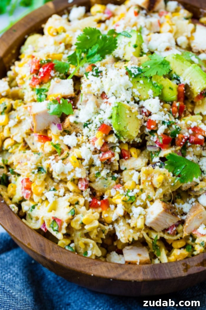 Zesty Elote Chicken Pasta Salad 3 A close-up of a wooden bowl filled with Elote Mexican Grilled Corn Pasta Salad with Chicken, highlighting the bowtie pasta, charred corn, tender chicken pieces, creamy avocado, and crumbled cotija cheese.