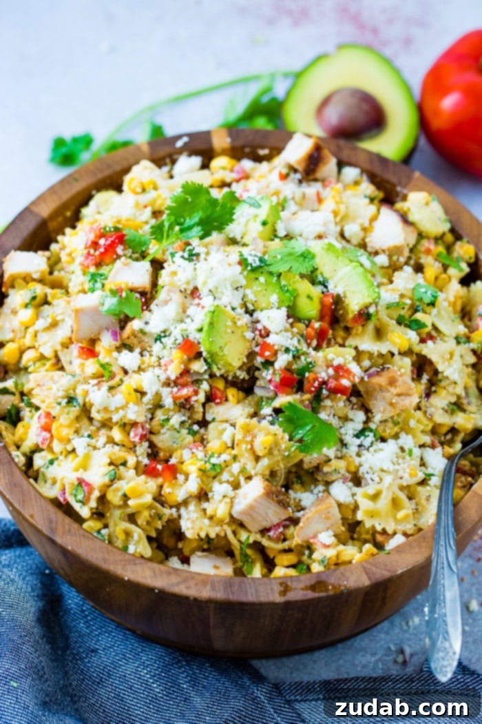 Zesty Elote Chicken Pasta Salad 4 A full wooden bowl of Elote Mexican Grilled Corn Pasta Salad with Chicken, showcasing the colorful ingredients including bowtie pasta, grilled corn, avocado, red bell peppers, cilantro, and cotija cheese.