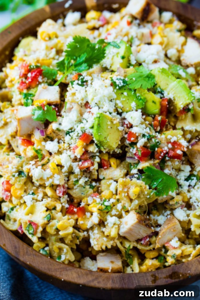 Zesty Elote Chicken Pasta Salad 5 A scoop of Elote Mexican Grilled Corn Pasta Salad with Chicken being lifted from a wooden bowl, showcasing the fresh, colorful ingredients and creamy dressing.