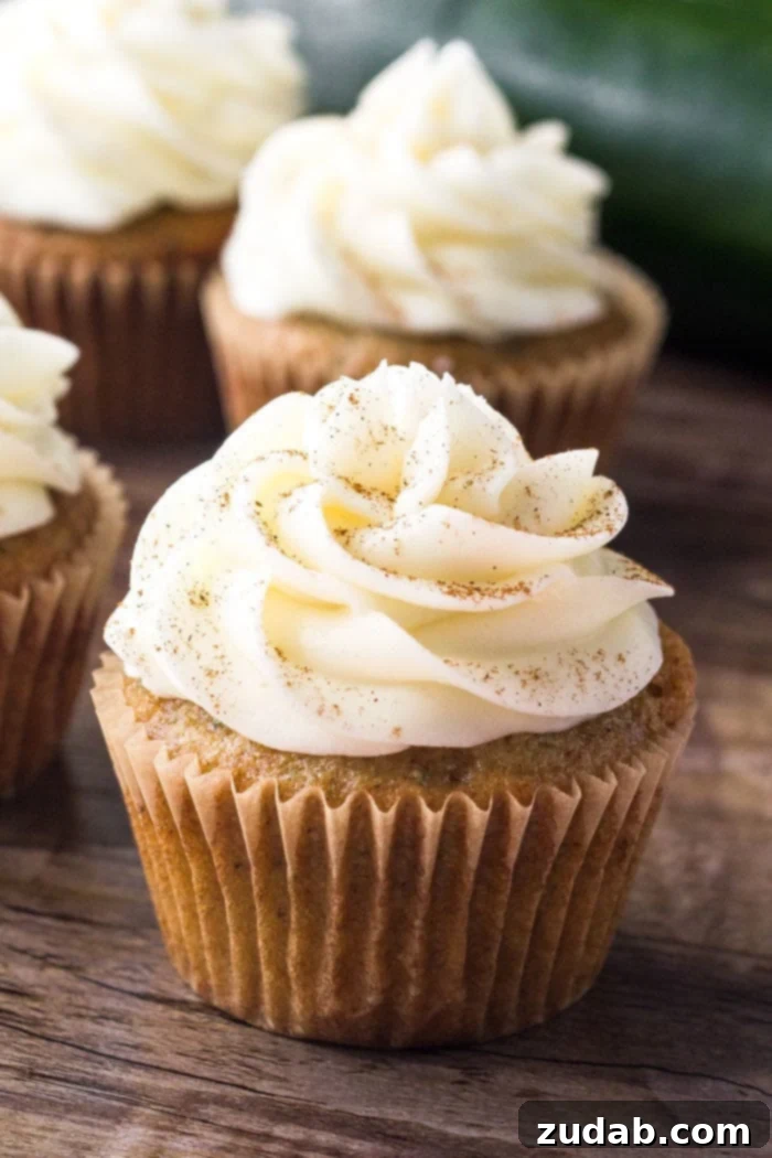 Cream Cheese Frosted Zucchini Delights 2 A beautifully baked zucchini cupcake, nestled in its wrapper, adorned with generous swirl of fluffy cream cheese buttercream frosting and a delicate sprinkle of cinnamon.