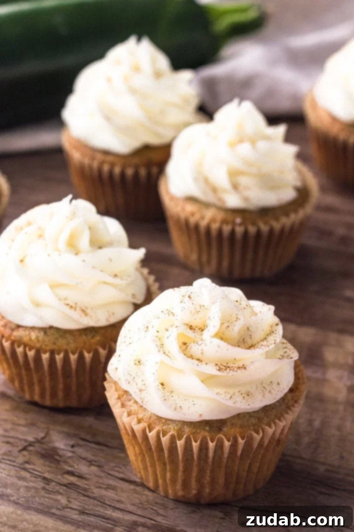 Cream Cheese Frosted Zucchini Delights 5 Close-up shot of individual zucchini cupcakes, beautifully topped with creamy cream cheese frosting and a dusting of cinnamon, invitingly presented.