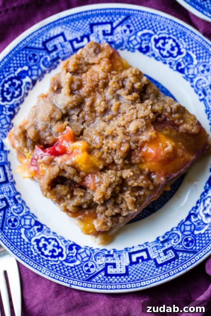 A single slice of golden-brown sugar peach pie bar, showcasing the juicy peach filling and crumbly topping, presented on an elegant blue and white plate.