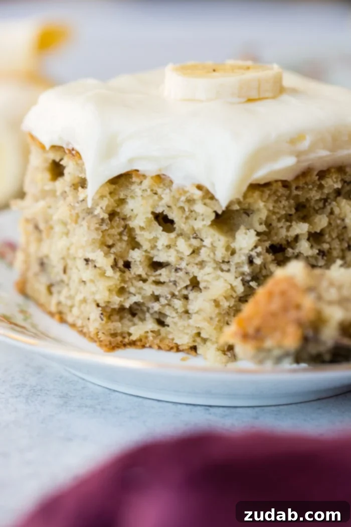 Perfectly Moist Banana Cake 2 A delectable slice of moist banana cake generously topped with cream cheese frosting, with a small bite taken out, showcasing its perfect texture.